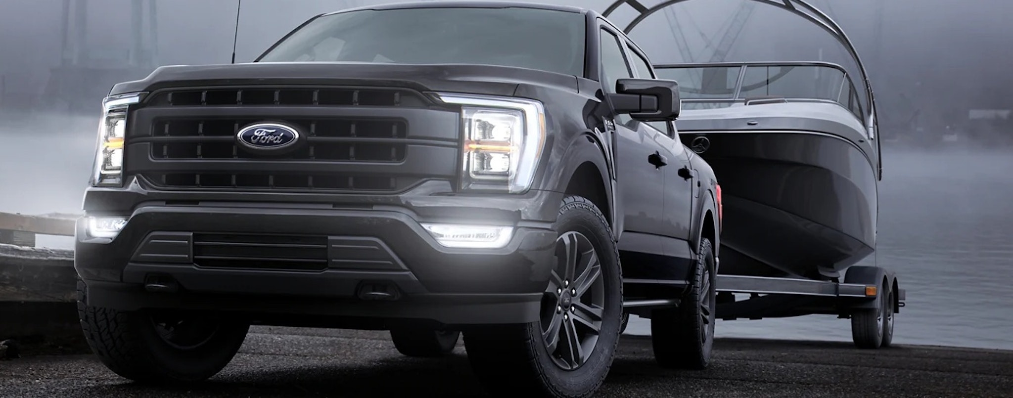 A black 2023 Ford F-150 is shown towing a boat out of a lake.