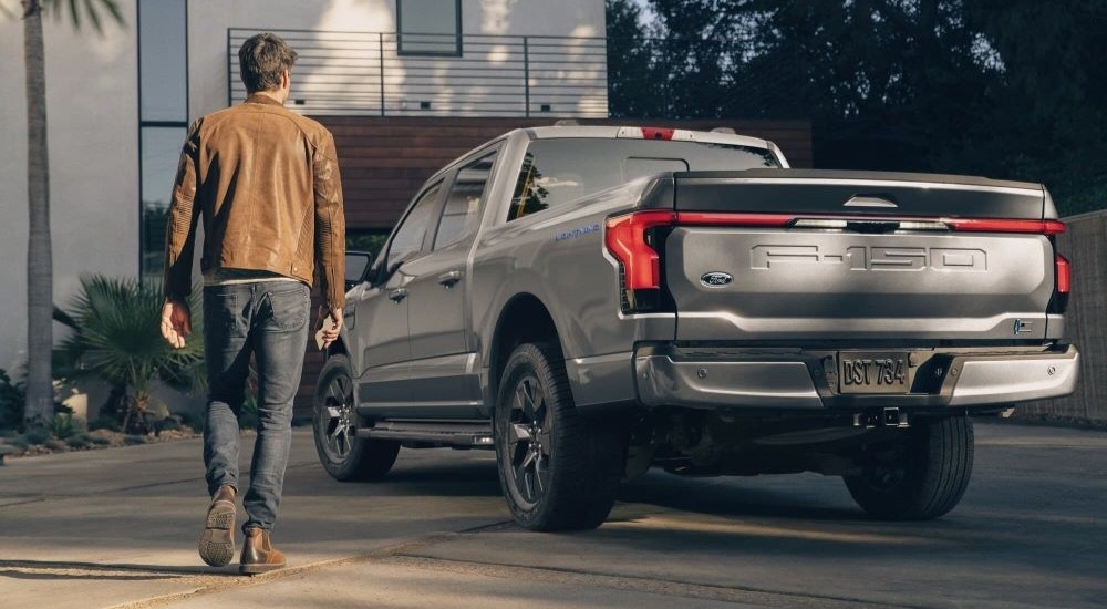 Rear angle view of a silver 2023 Ford F-150 Lightning parked on a driveway after visiting a Ford F-150 Lightning dealer.