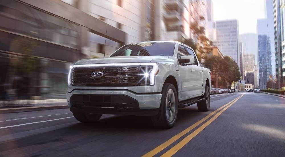 A white 2023 Ford F-150 Lightning driving through a city.