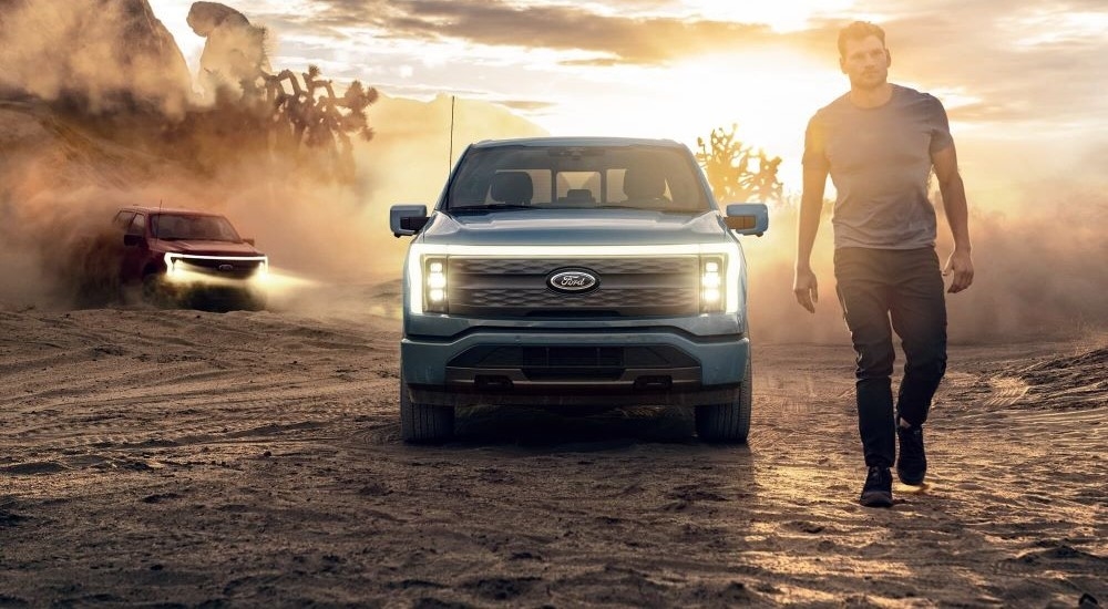 Front view of a man walking from a blue 2023 Ford F-150 Lightning parked off-road.