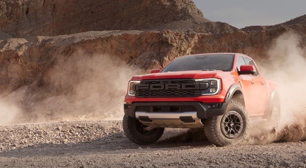 A red 2024 Ford Ranger Raptor is shown kicking up dust off-road after leaving a Ford truck dealer.