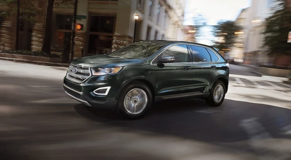 A green 2016 Ford Edge is driving on a city street.