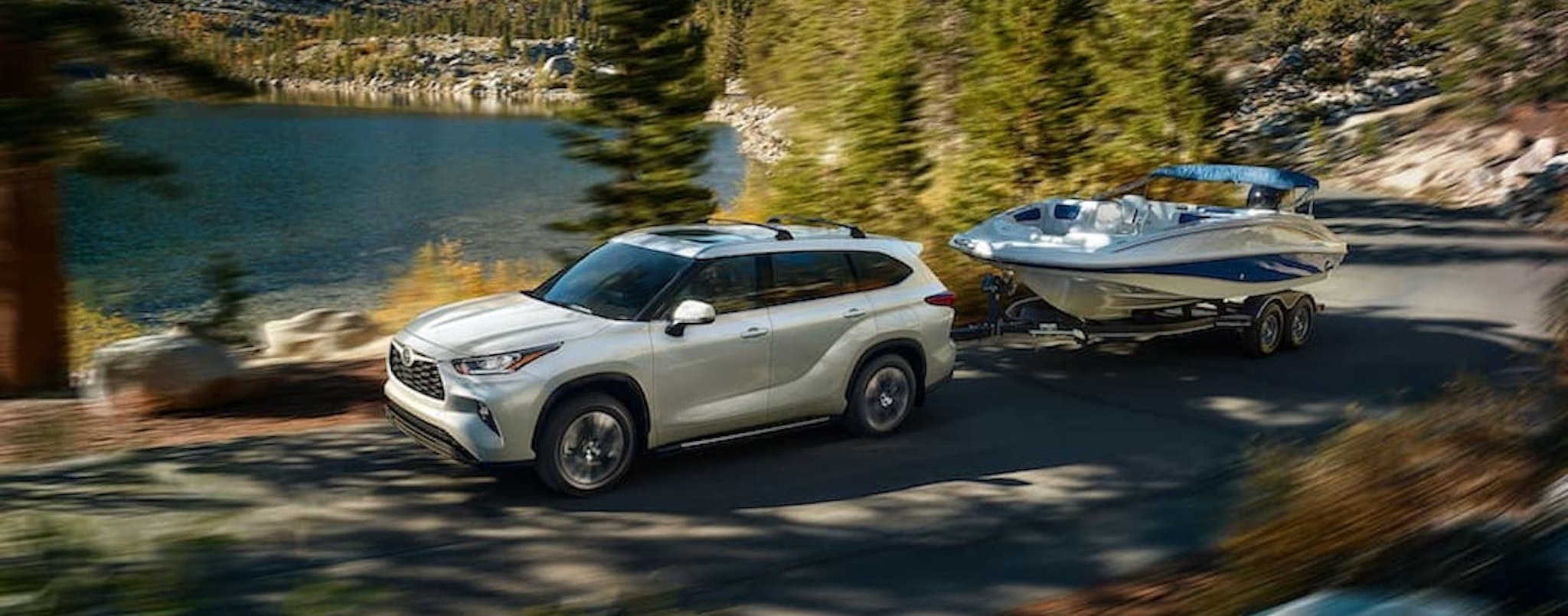 A white 2022 Toyota Highlander is shown from the side while towing a boat.