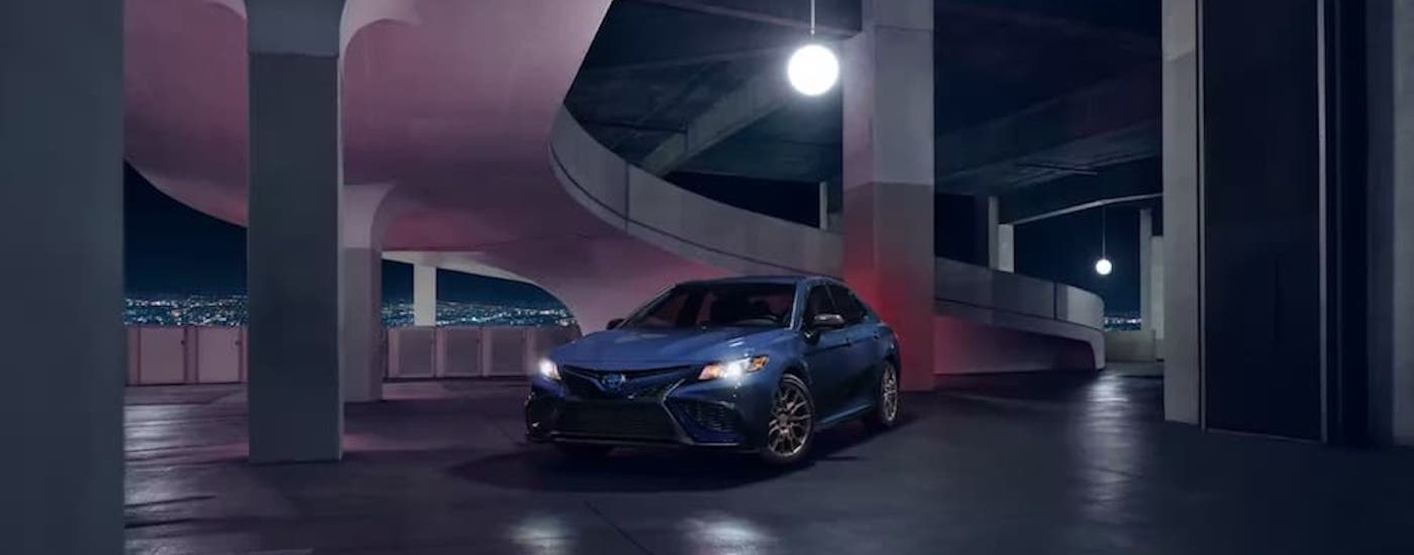 A blue 2023 Toyota Camry Nightshade is driving through a parking garage.