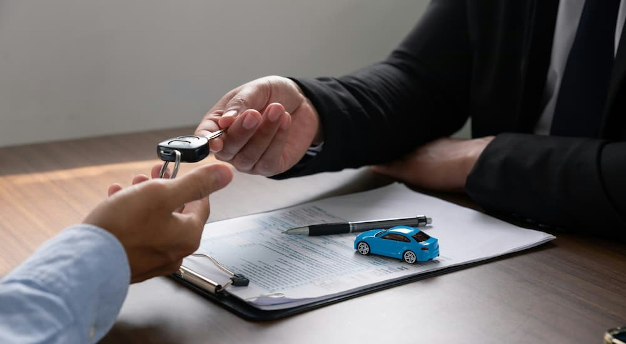 A salesman is shown handing a carkey to customer.