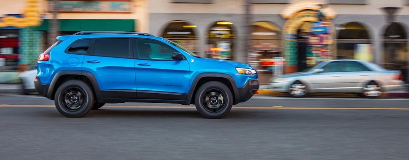 A blue 2020 Jeep Cherokee is shown driving on a city street after viewing a used Jeep for sale.