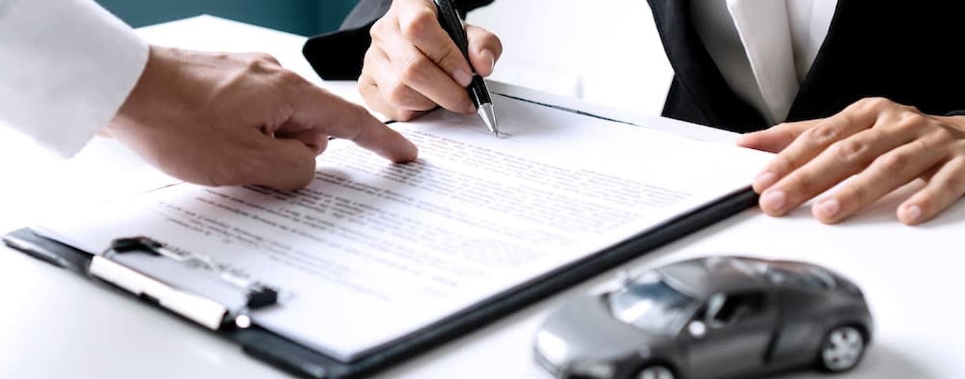 A person is shown pointing at a document being signed at a bad credit car dealership near me.