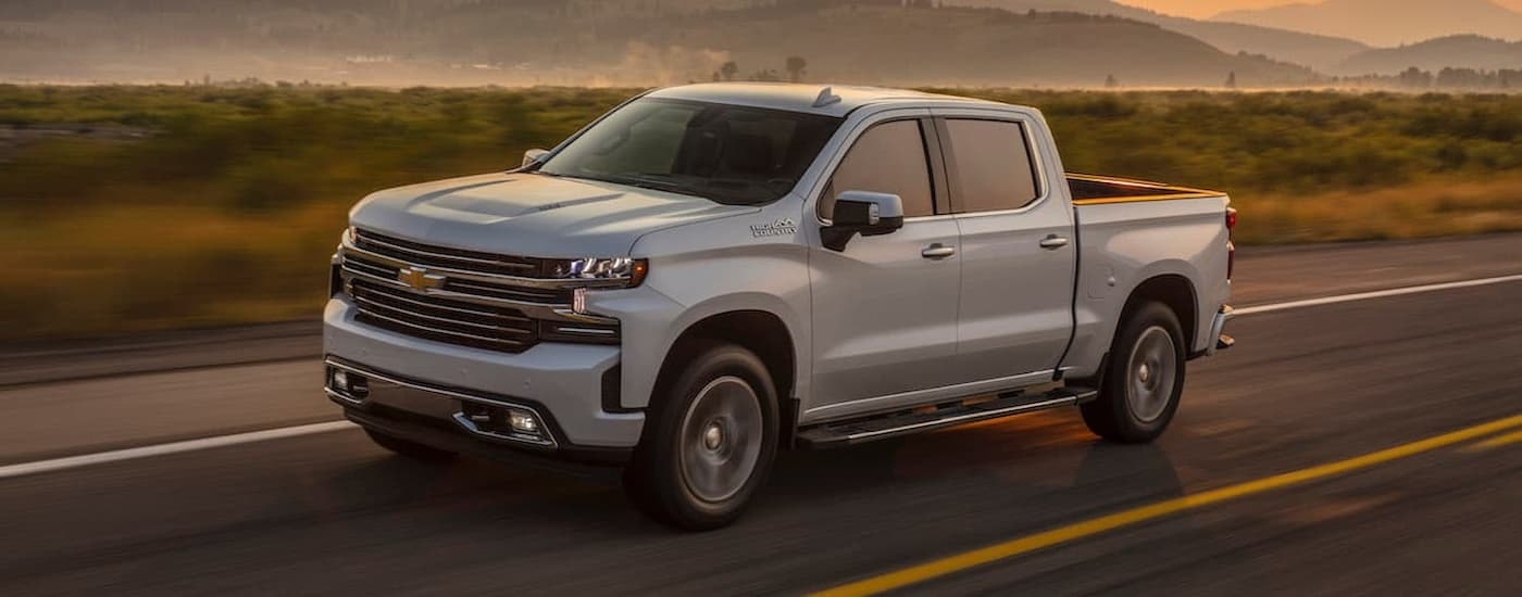 A white 2019 Chevy Silverado 1500 High Country is shown driving on an open road after viewing used Chevy trucks for sale.