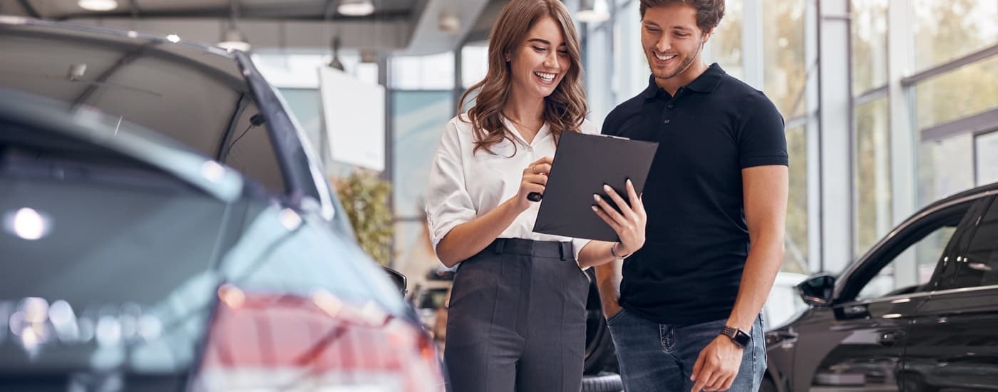 A man is shown speaking to a saleswoman at a dealership about different vehicles.