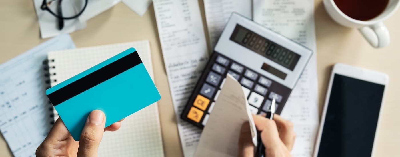 A person is shown holding a blue credit card while going over paperwork for bad credit car loans near Newport, NH.