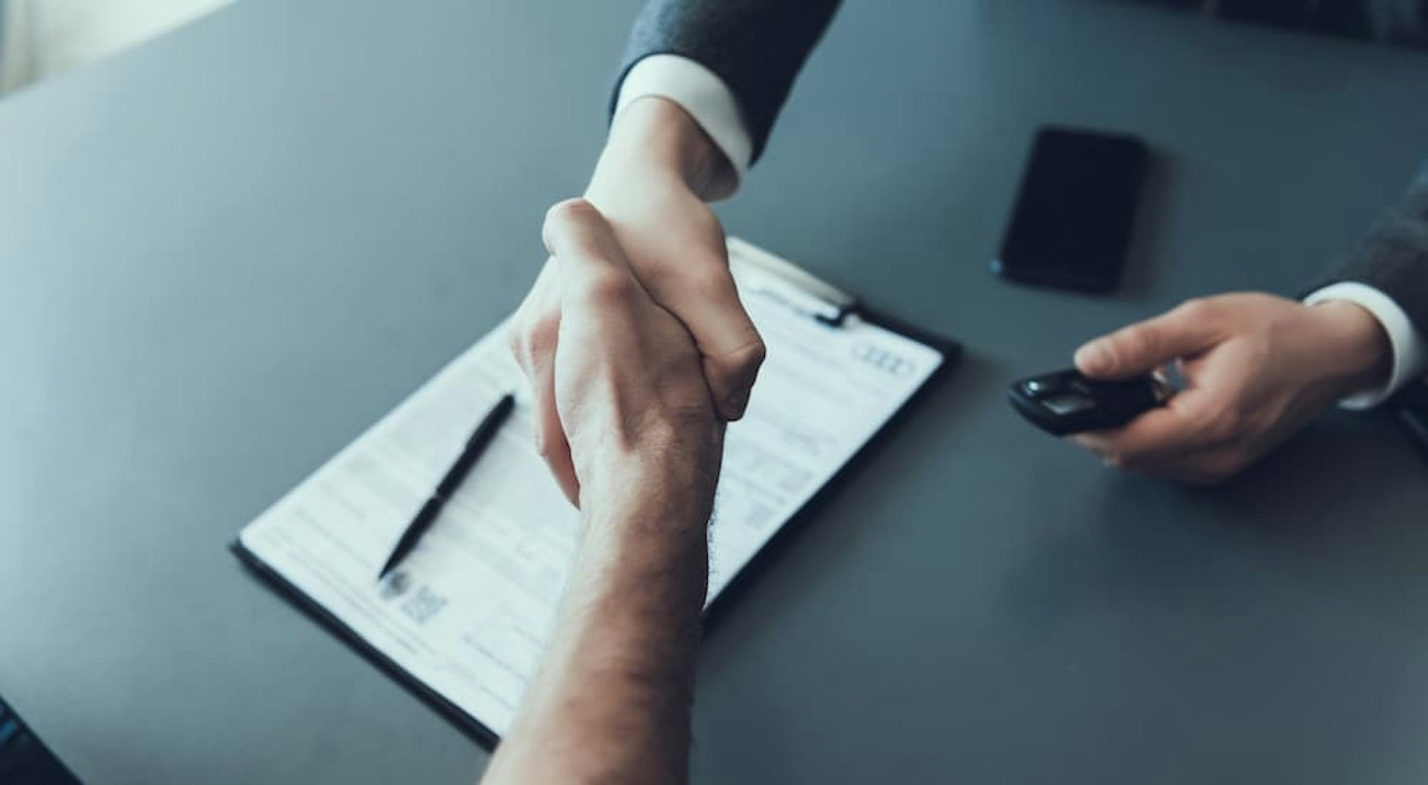 Two people are shown shaking hands over some paperwork.