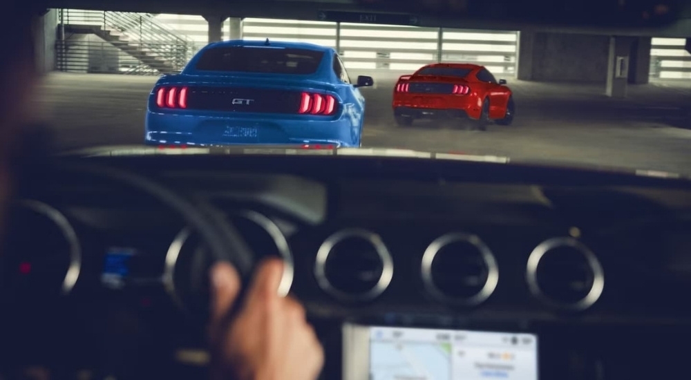 A blue and a red 2023 Ford Mustang GT are shown in a parking garage.