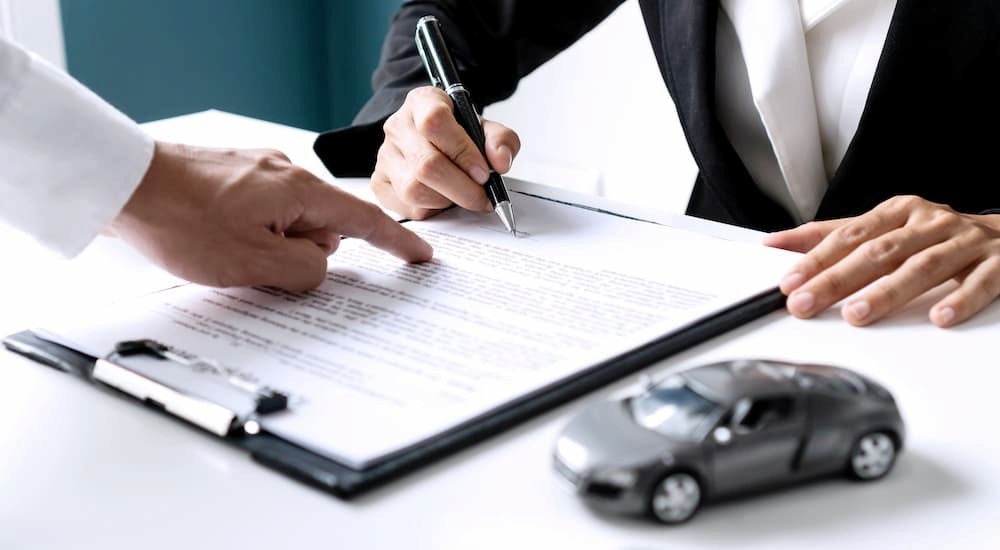 Someone is shown filling out paperwork at a car dealership.