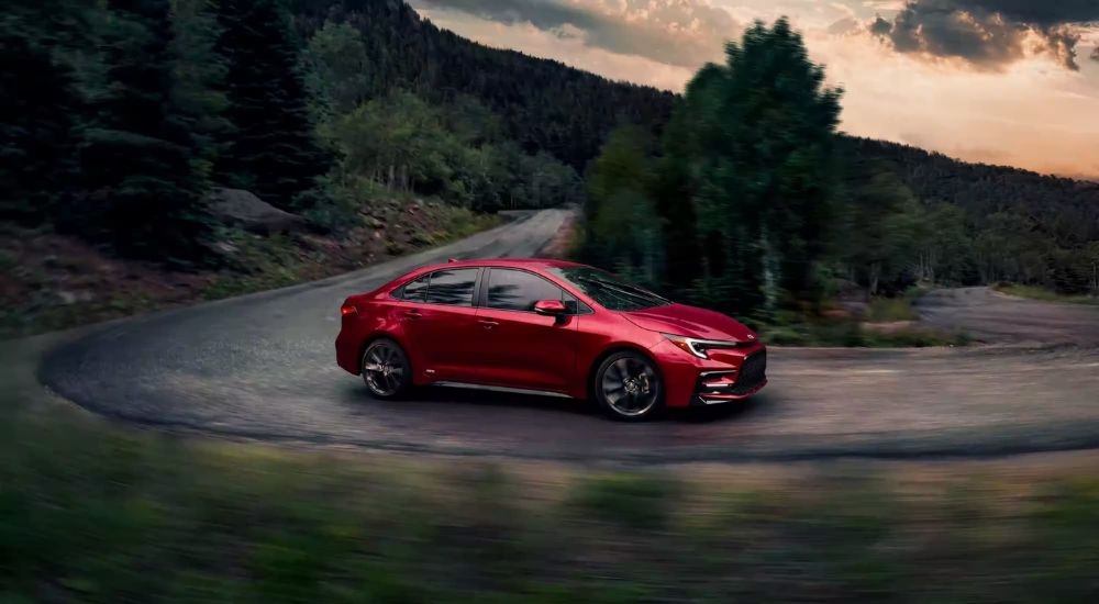 A red 2023 Toyota Corolla is shown from the side on a winding road.