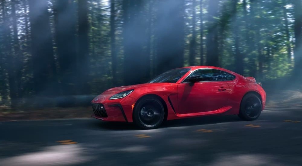 A red 2024 Toyota GR86 is shown from the side while driving through the forest.