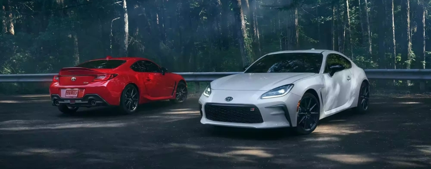 A red and a white 2024  Toyota GR86 are shown parked near trees.