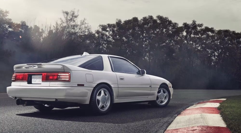 A white 1990 Toyota Supra is shown parked on a racetrack.