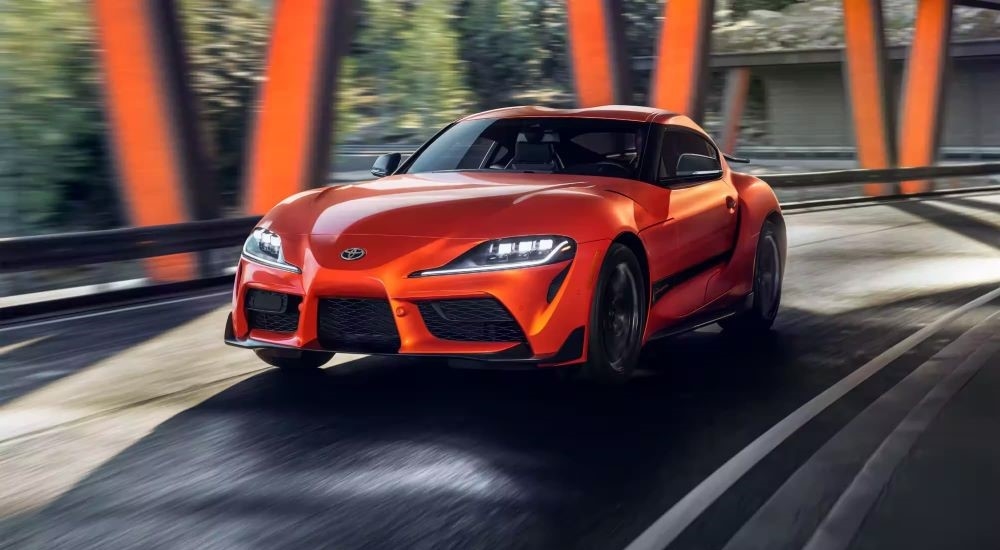 An orange 2024 Toyota Supra 45th Anniversary Edition is shown rounding a corner.