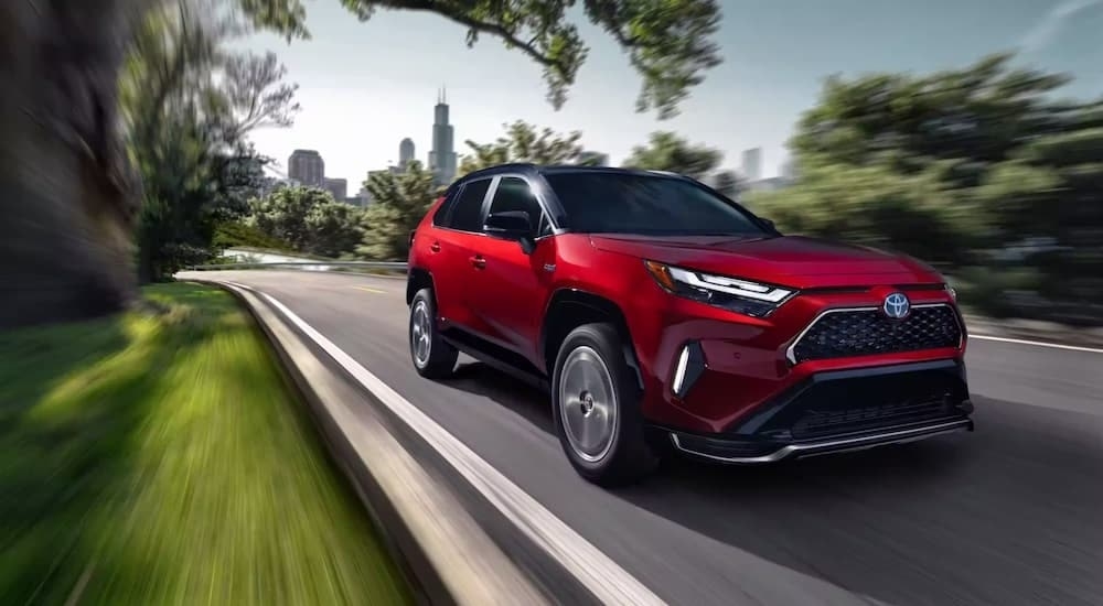 A red 2023 Toyota RAV4 Prime driving near a city.
