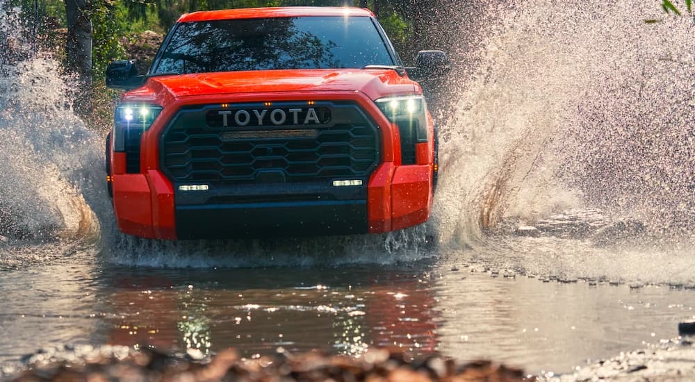 An orange 2024 Toyota Tundra TRD is shown from the front while driving through mud.