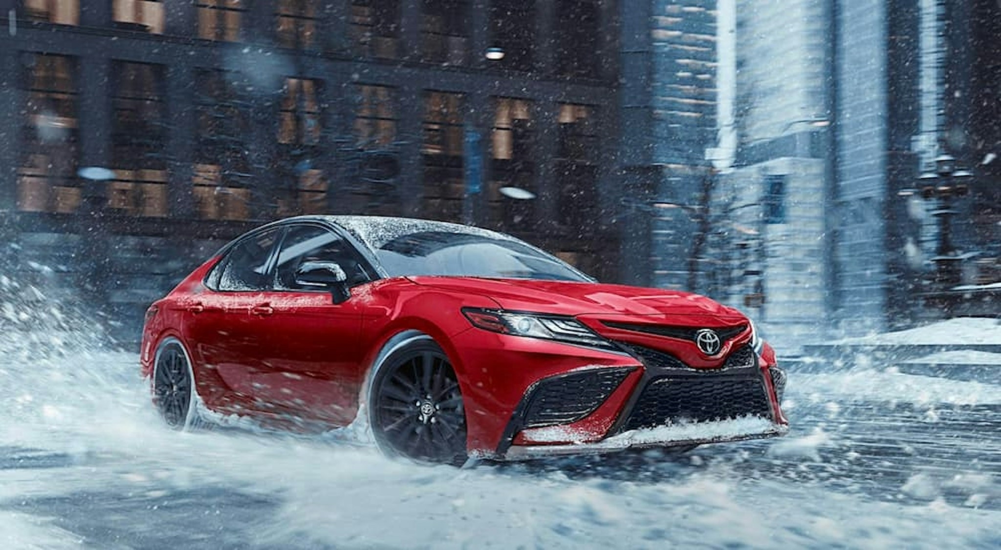 A red 2020 Toyota Camry driving in the snow.