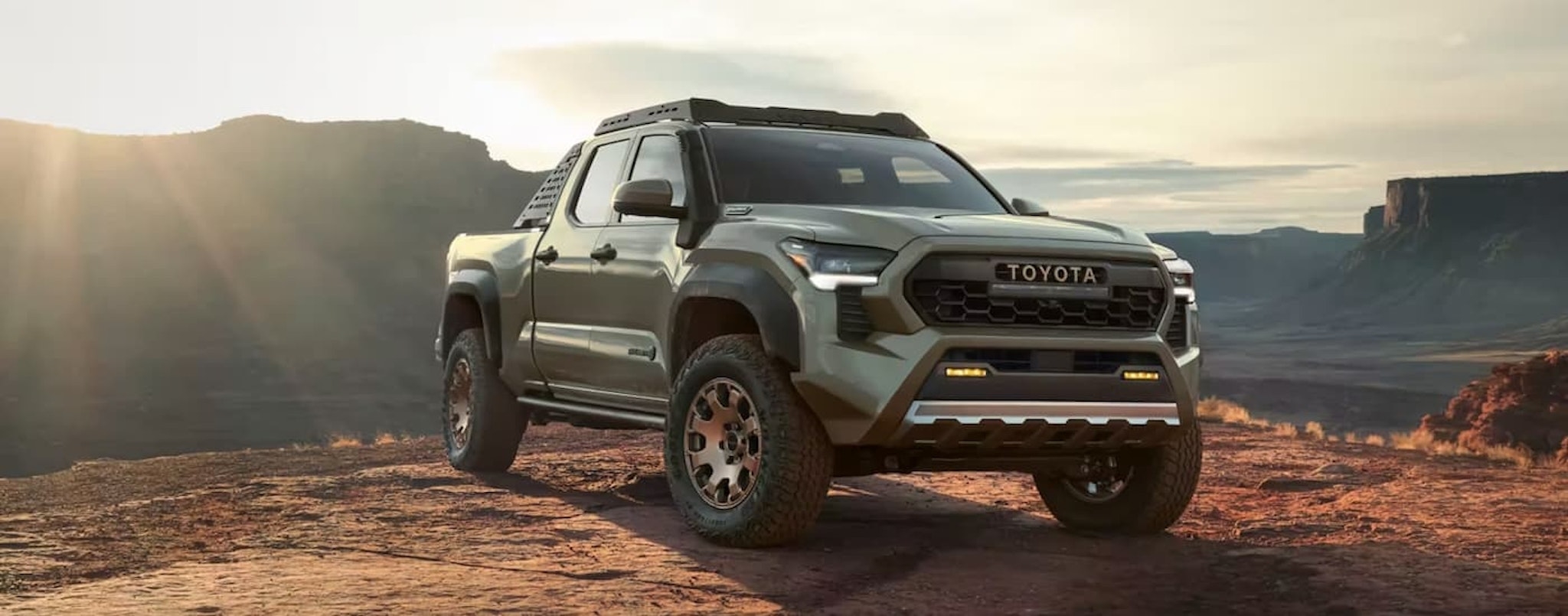 A green 2024 Toyota Tacoma is shown parked overlooking a mountain view.