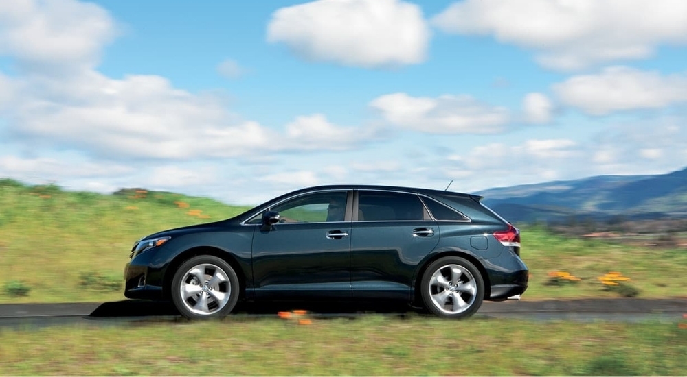 A used Toyota for sale, a black 2015 Toyota Venza, is shown from the side driving on an open road.