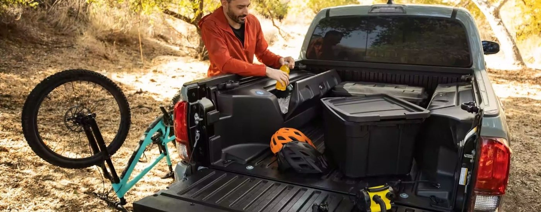 A person is shown holding a drink near a grey 2023 Toyota Tacoma SR5 Trail Edition.