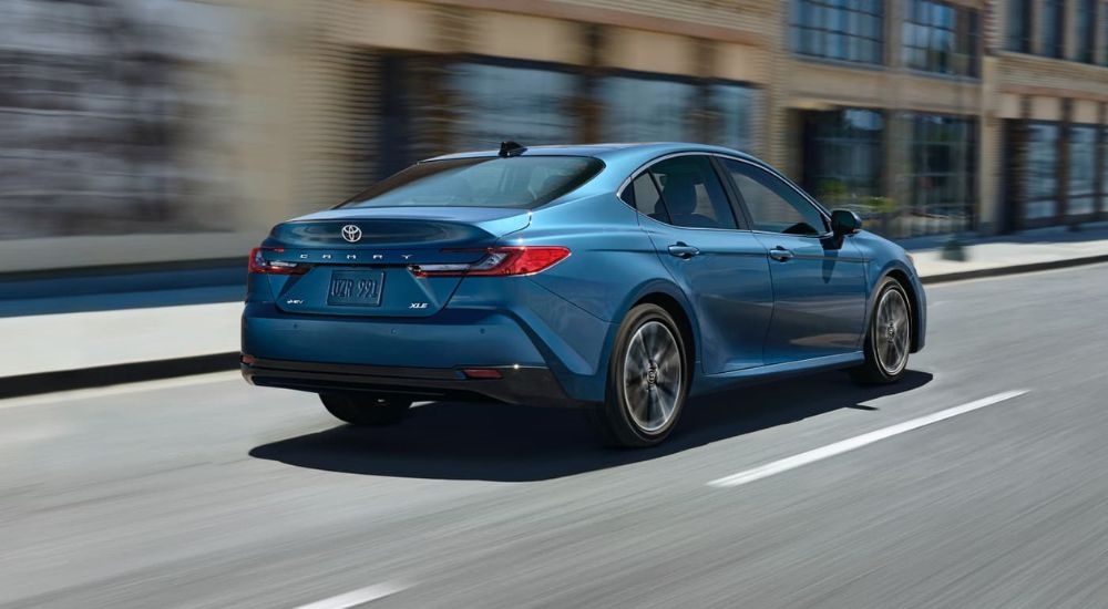 A blue 2025 Toyota Camry XLE is shown from the rear driving on a city street.