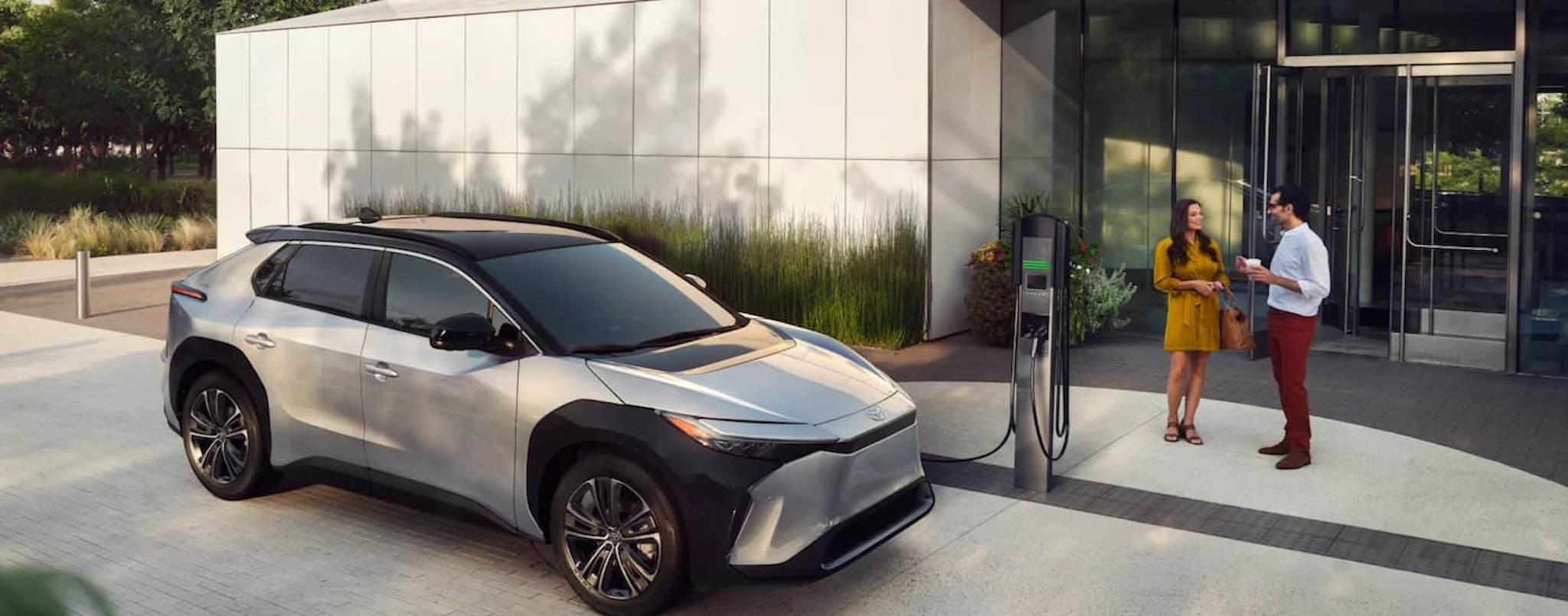 A silver 2023 Toyota bz4X is shown charging outside of an office building.