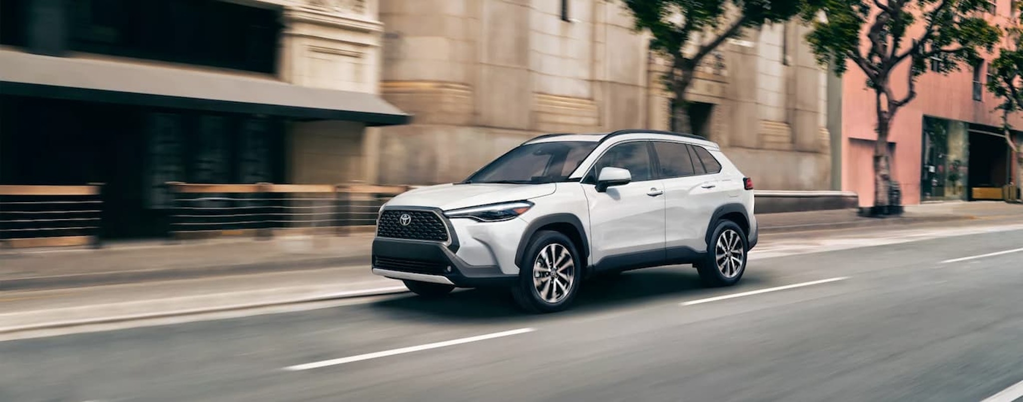 A blue 2023 Toyota Corolla Cross XLE is shown from the side driving up a steep city street.