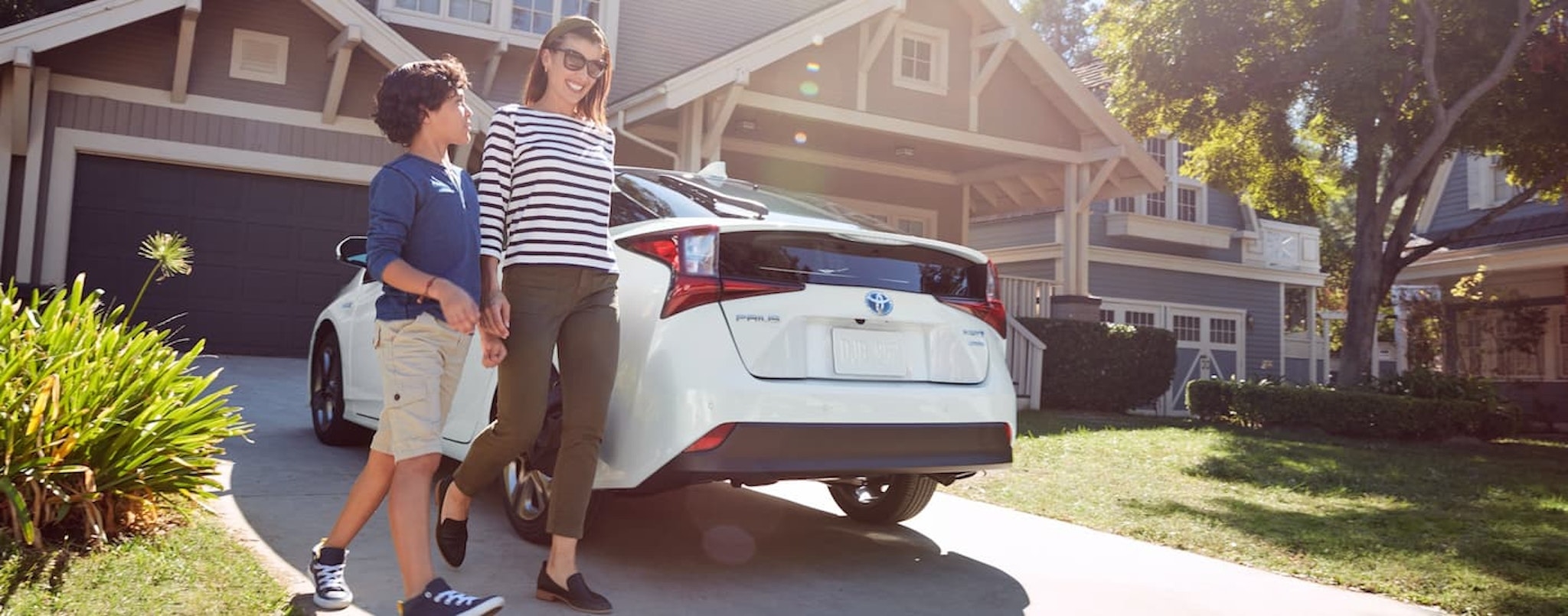 A family is shown walking next to a white 2021 Toyota Prius parked in a driveway.