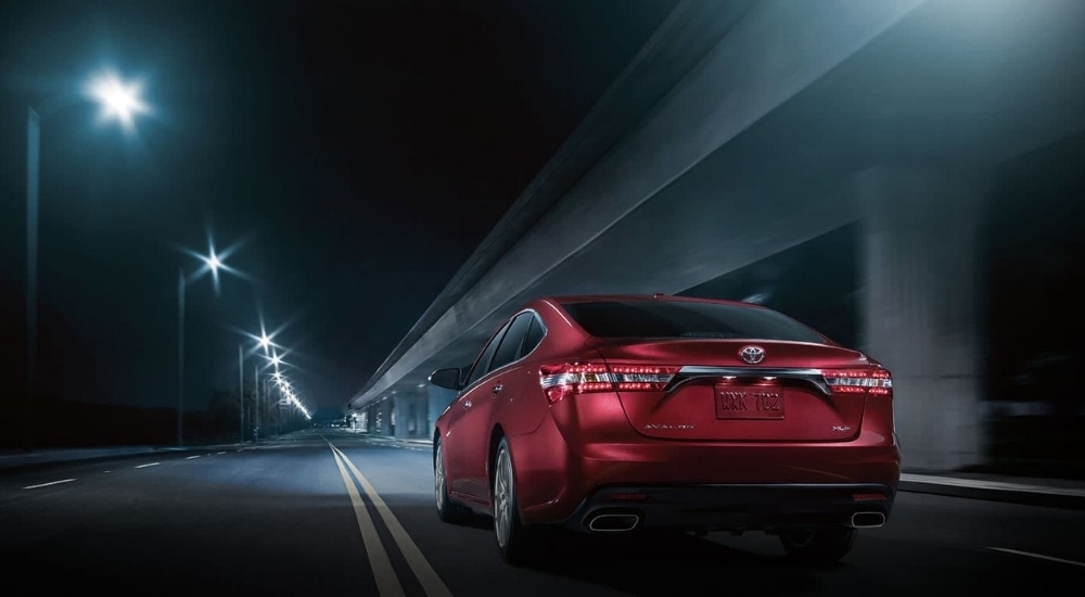 A red 2015 Toyota Avalon is shown driving on a city street at night.