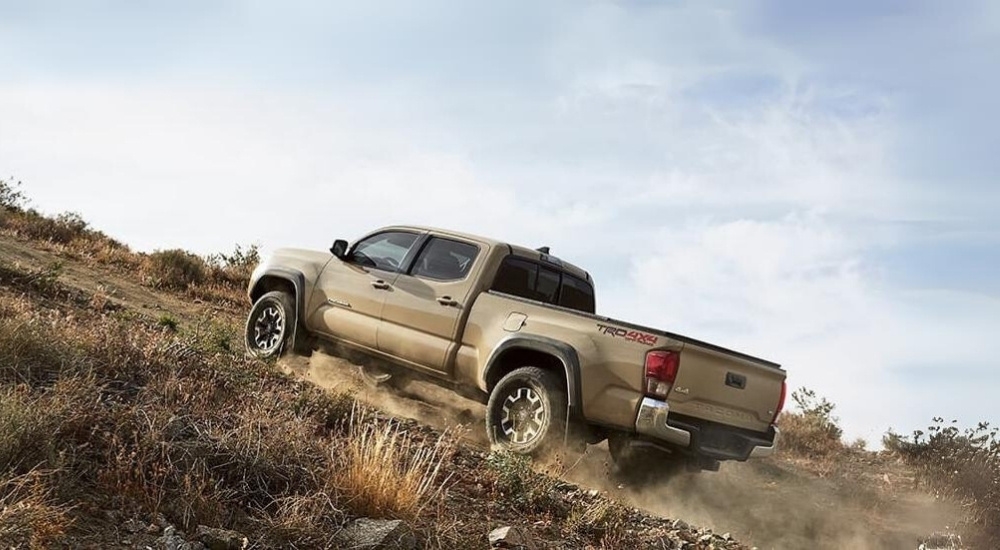 A tan 2016 Toyota Tacoma TRD is shown driving to a used Toyota dealer.