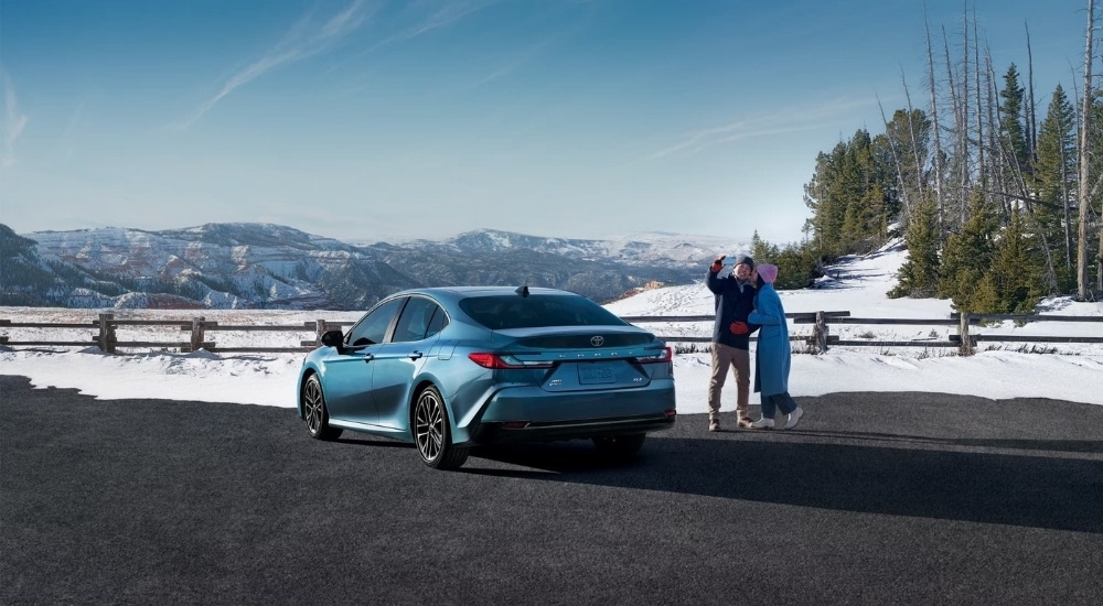 People are shown taking a selfie near a blue 2025 Toyota Camry XLE.