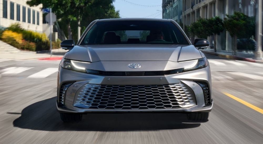 A grey 2025 Toyota Camry XSE is shown from the front driving on a city street.