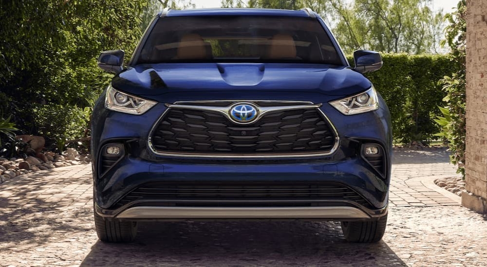 A dark blue 2023 Toyota Highlander Hybrid is shown from the front parked beneath a stone archway.