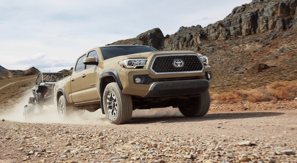 A tan 2019 Toyota Tacoma is shown off-roading on a rocky road.