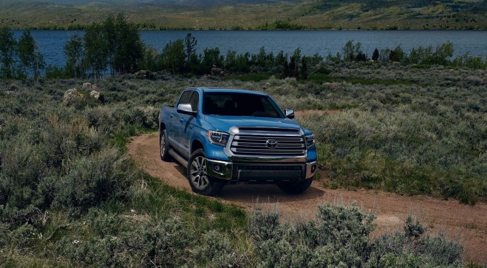 A blue 2021 Toyota Tundra Limited is shown driving on a dirt road near a lake.