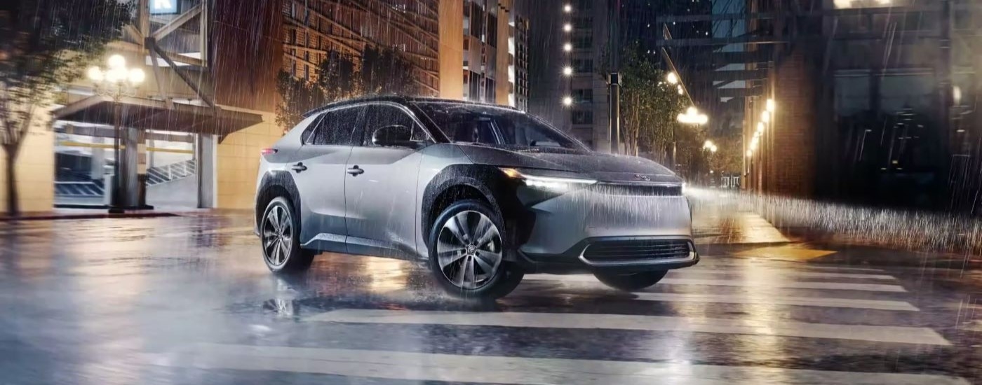 A silver 2023 Toyota bZ4X Limited is shown driving on a city street in the rain.