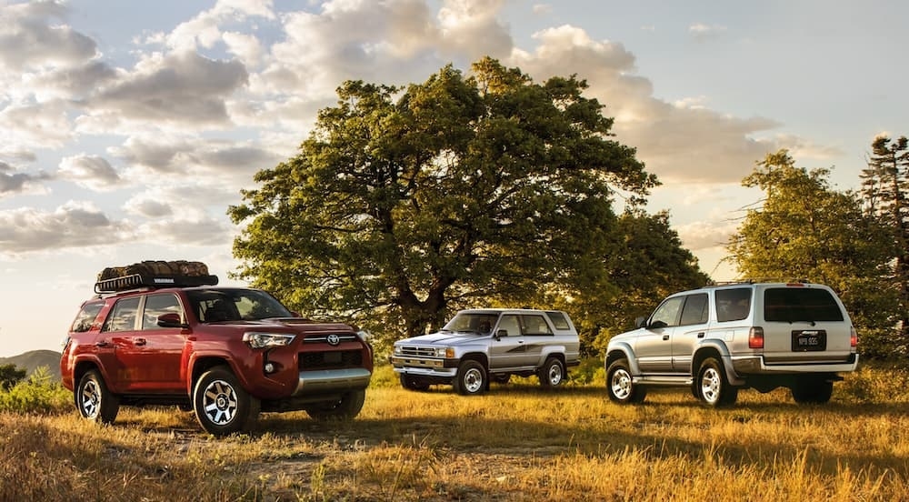 A red and two silver Toyota 4Runners of various years parked in an open field.