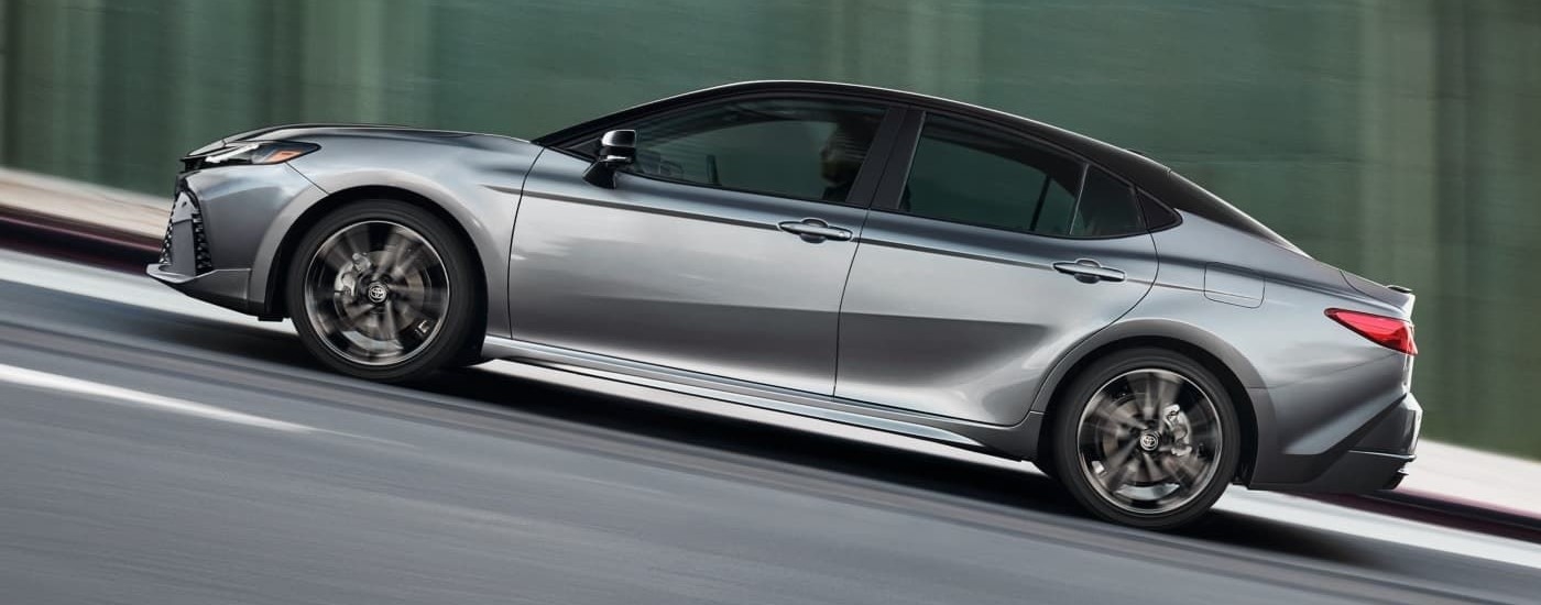 A silver 2025 Toyota Camry is shown from the side against a blurred background.