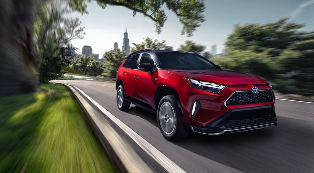 A red 2022 Toyota RAV4 Prime driving near a city.