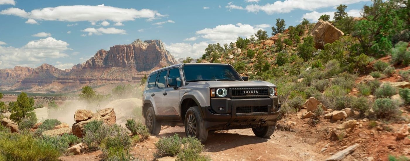 A silver 2024 Toyota Land Cruiser is shown driving on a dusty trail.