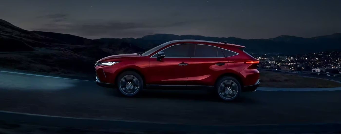 A red 2023 Toyota Venza Nightshade Edition is shown from the side driving past a city at night.