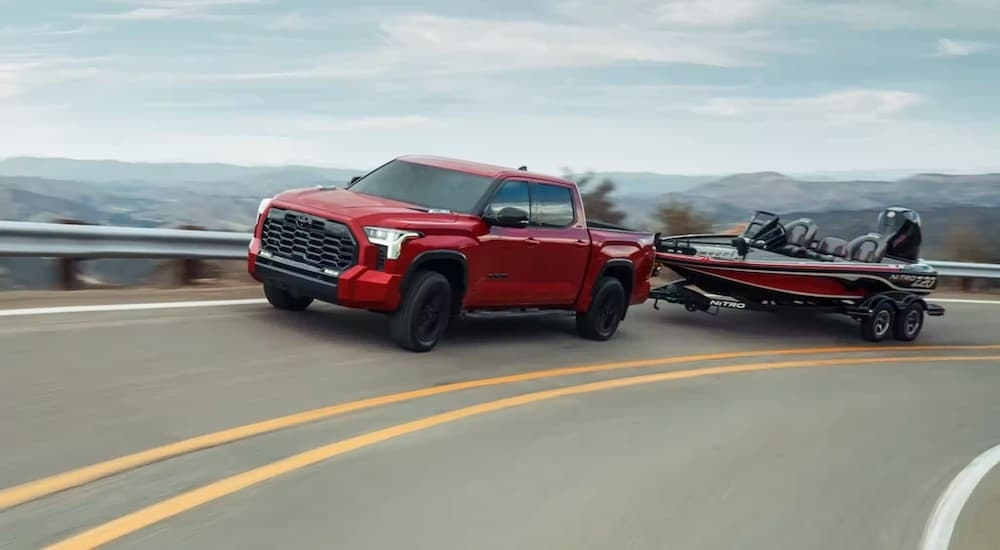 An orange 2024 Toyota Tundra is shown from the front at an angle while towing a boat.