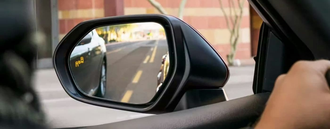 A close up shows the blind spot monitoring icon on the mirror of a red 2023 Toyota Camry.