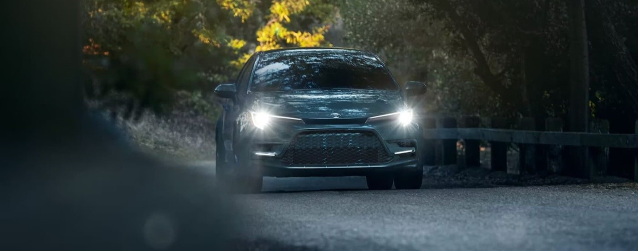 A blue 2023 Toyota Corolla XSE is shown driving on a tree-lined road.