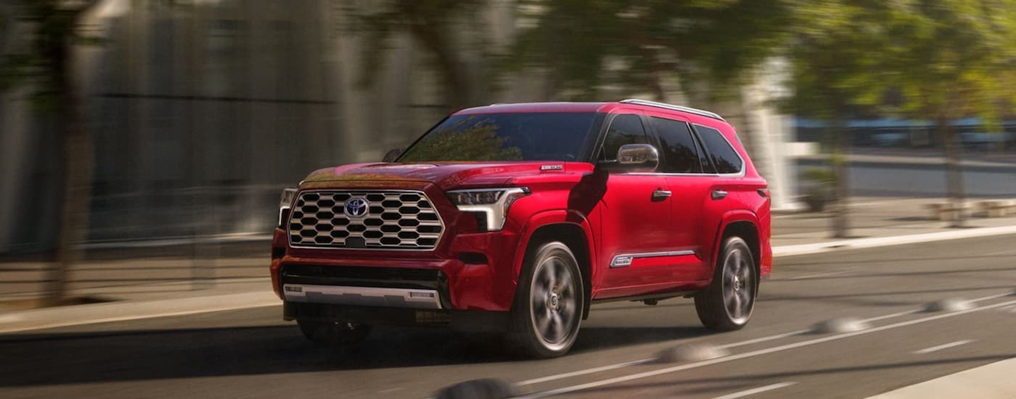 A red 2024 Toyota Sequoia Capstone is shown driving on a city street.