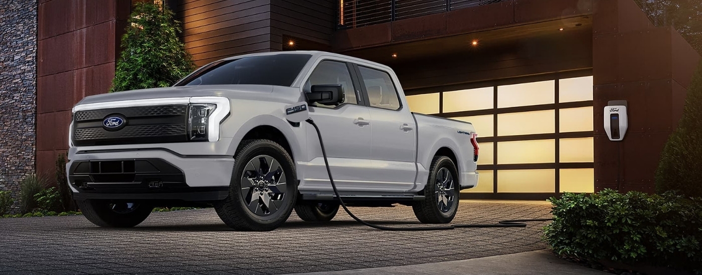 A white 2024 Ford F-150 Lightning for sale near Keene is parked in front of a garage.